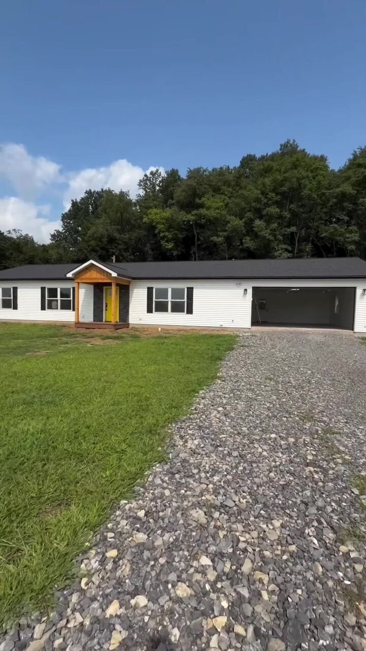New single-story home with a black garage door at the end of a gravel drive